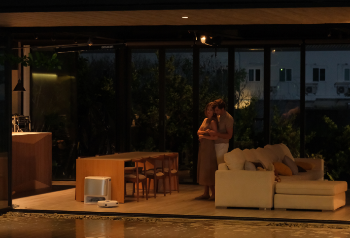 Two people embrace in a living room while the Narwal Freo Z Ultra robot vacuum cleans nearby.