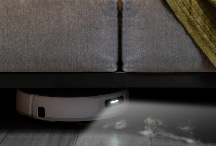 Narwal Freo Z Ultra robot vacuum cleaning under a sofa, with dust being sucked into the device's cleaning path.